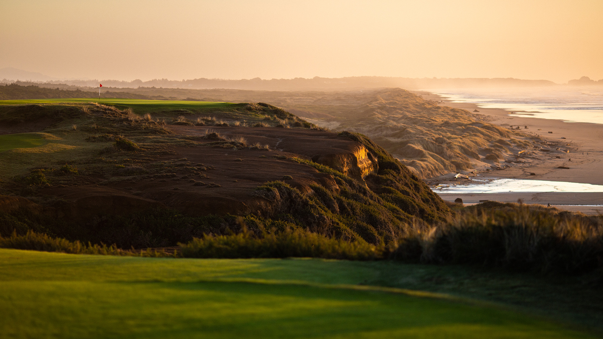 A clifftop green at Bandon Dunes at golden hour, red flag against the Pacific